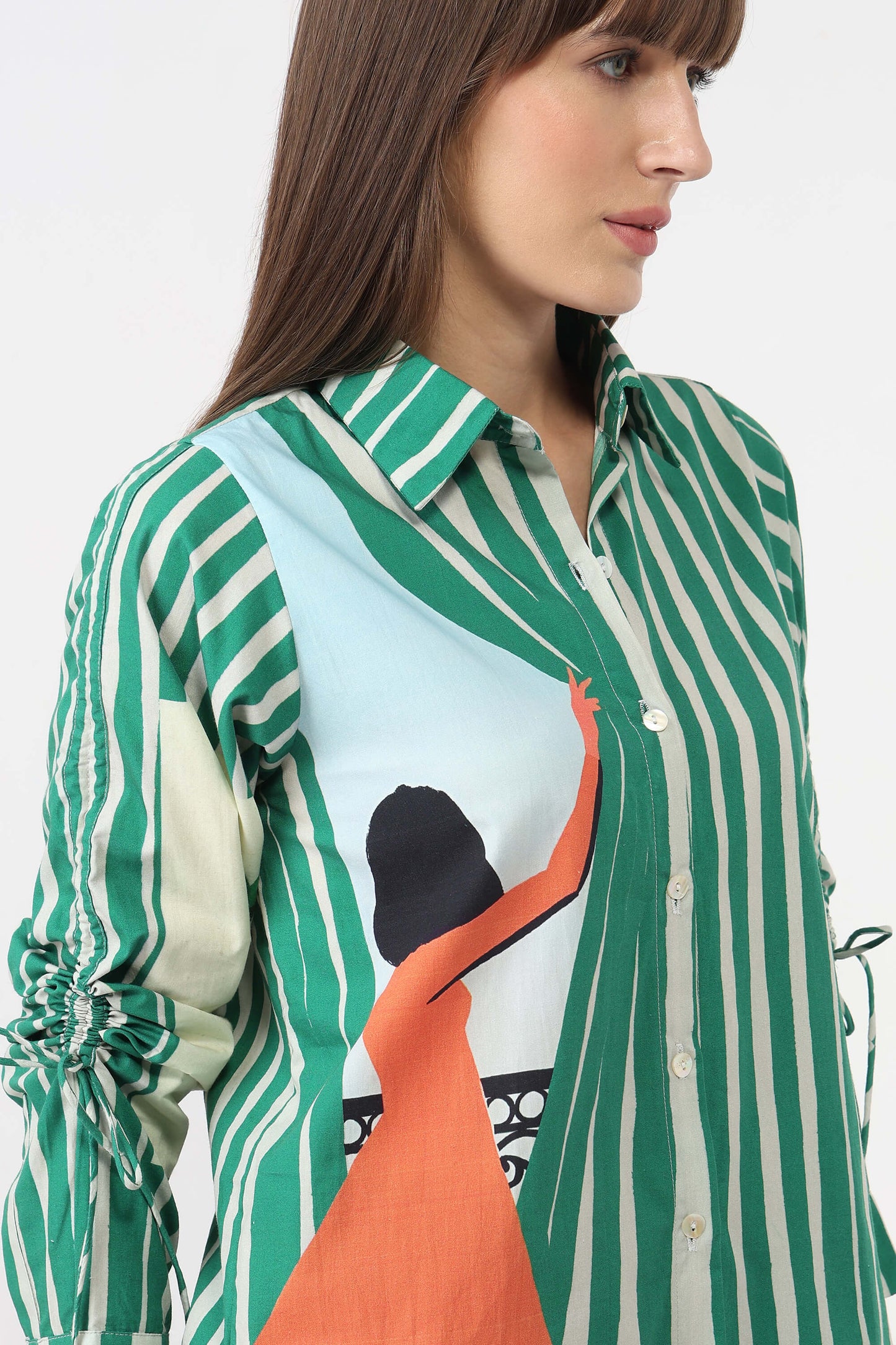A woman wearing a green and white vertically striped button-up shirt with a large abstract graphic print on the front in light blue, orange, and black, photographed against a plain light background.