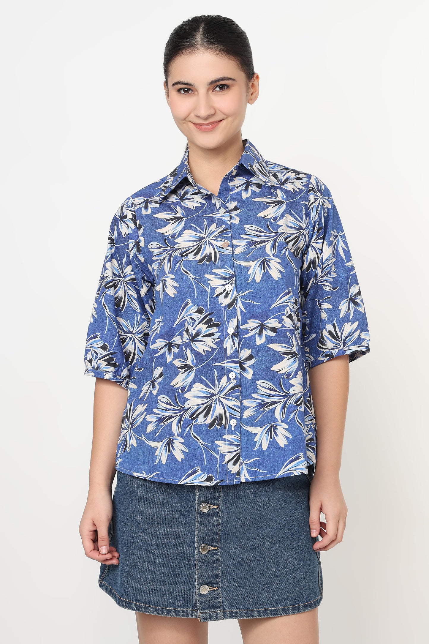 Woman wearing a blue floral shirt and denim skirt on a white background