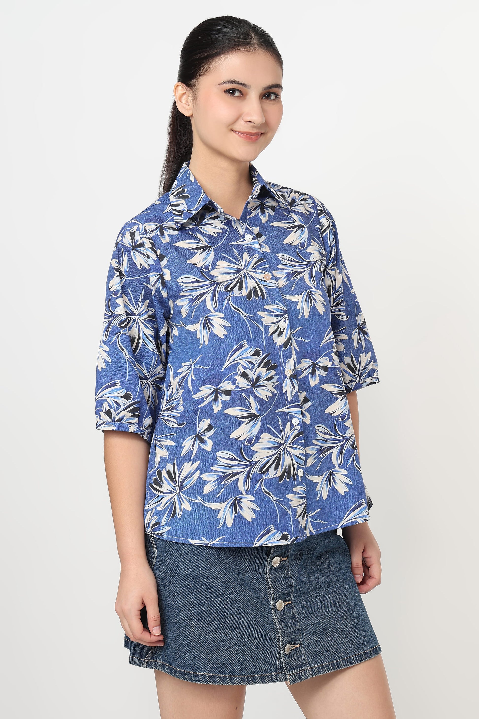 Woman wearing a blue floral shirt and denim skirt on a white background
