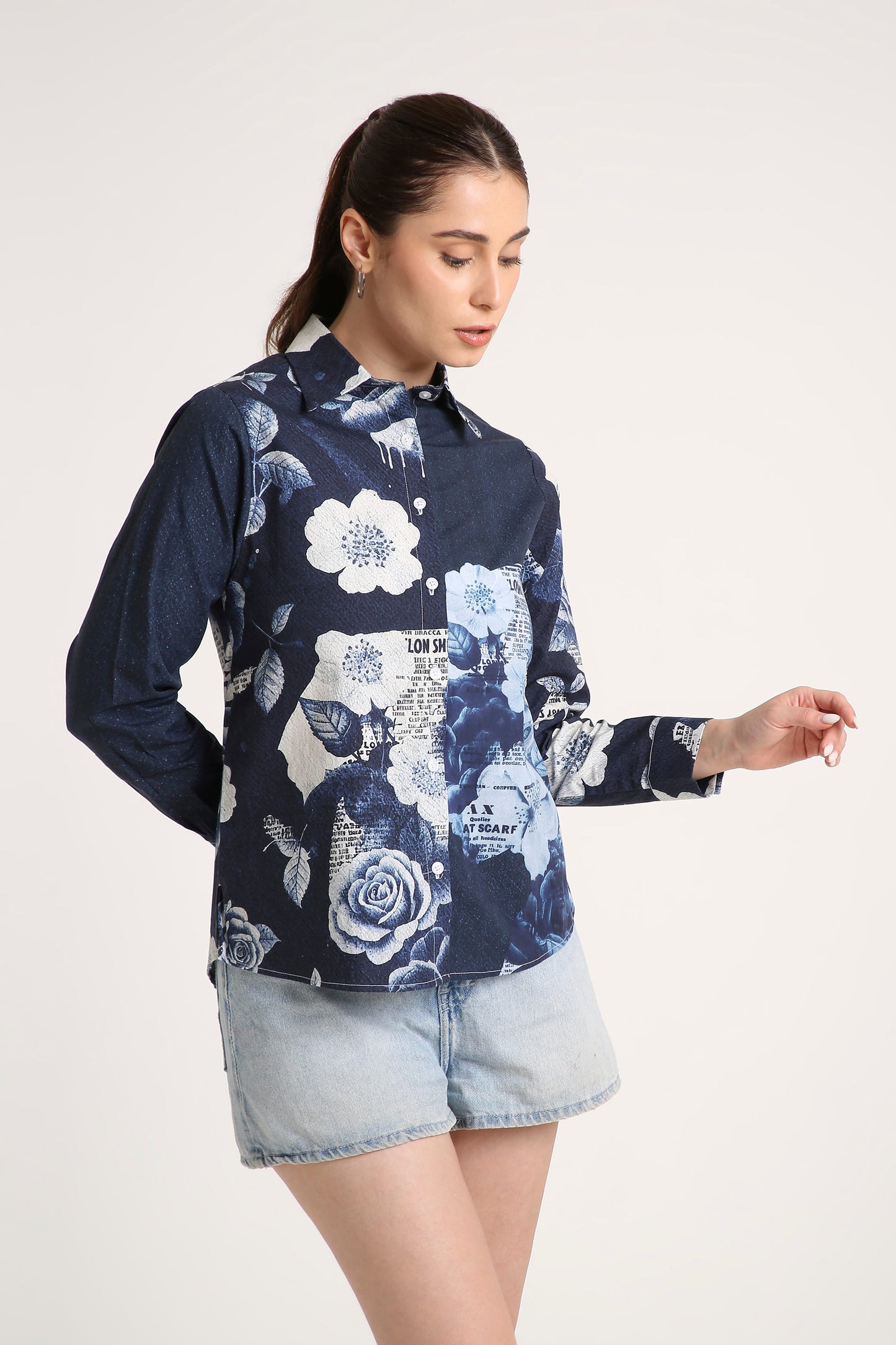 A woman wearing a navy blue long-sleeve button-up shirt with a white and light blue floral print, paired with denim shorts, against a plain light background.