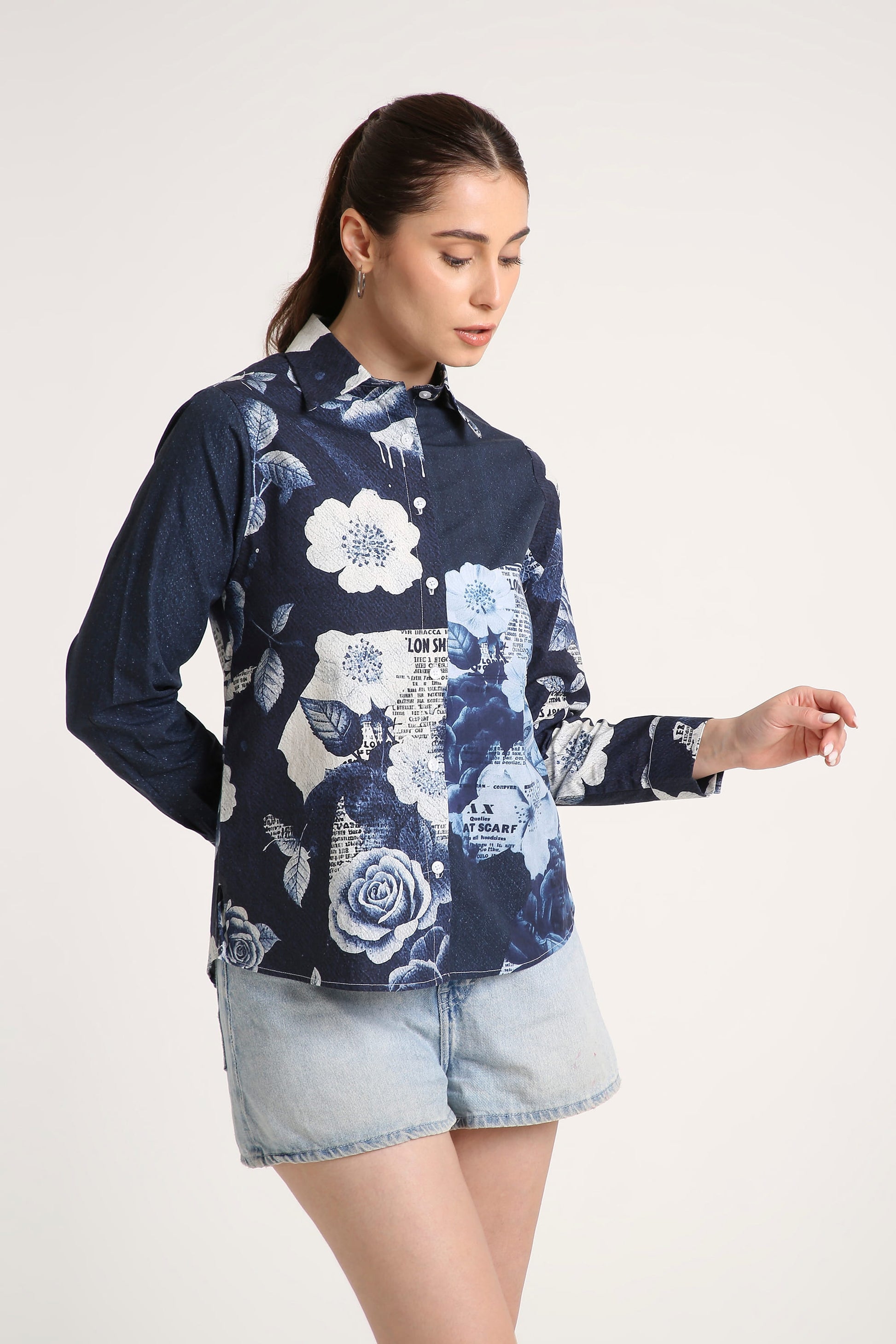 A woman wearing a navy blue long-sleeve button-up shirt with a white and light blue floral print, paired with denim shorts, against a plain light background.