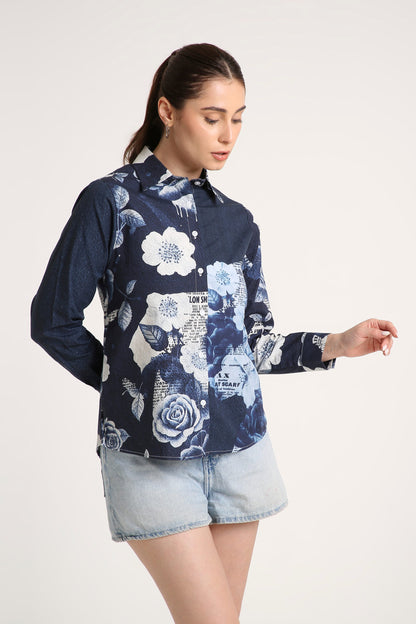 A woman wearing a navy blue long-sleeve button-up shirt with a white and light blue floral print, paired with denim shorts, against a plain light background.