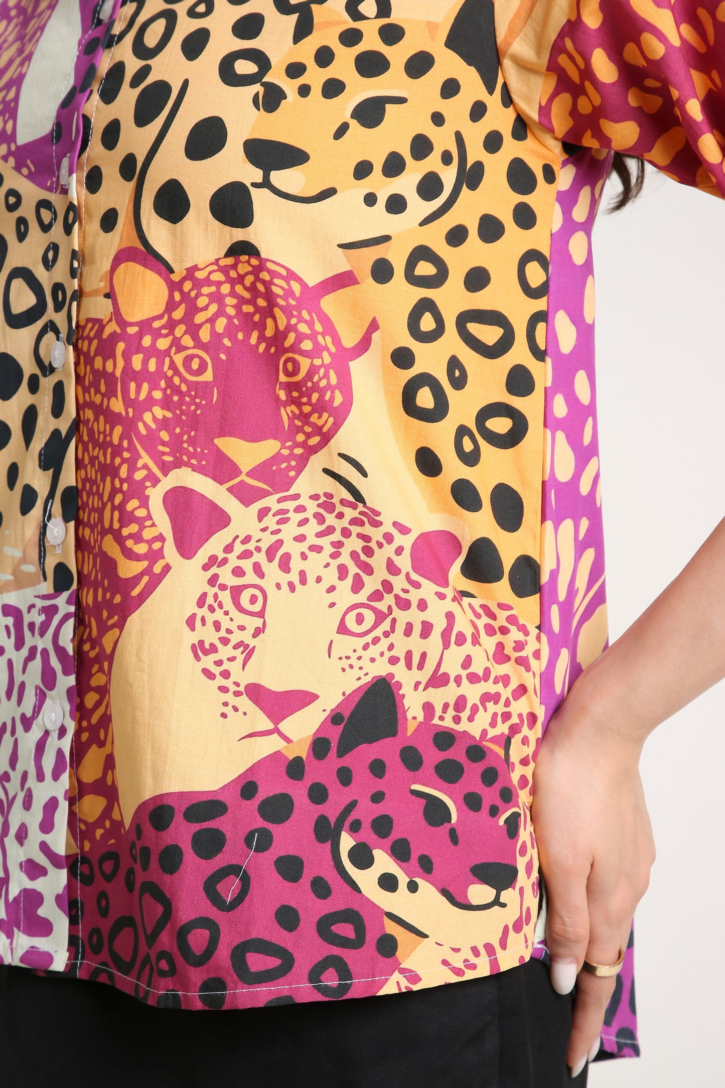 A close-up of a short-sleeve top featuring a vibrant print of two leopards in pink and yellow with black leopard spots, worn by a model.