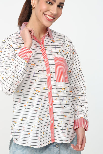 A woman wearing a long-sleeve button-up shirt with thin black horizontal stripes, a small multicolor animal print, and coral pink striped accents on the collar, placket, cuffs, and chest pocket, paired with light blue jeans against a plain white background.