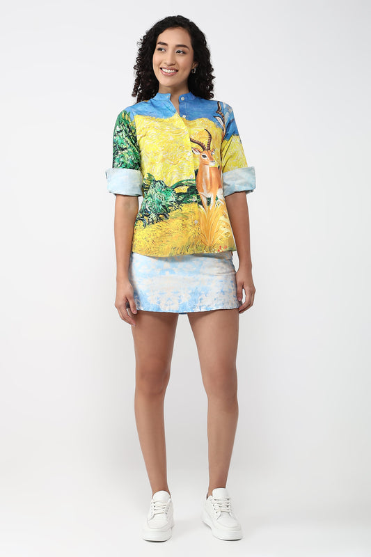 A woman modeling a matching short-sleeve button-up shirt and mini skirt set with a vibrant, multicolor landscape print featuring a deer, on a light gray studio background.