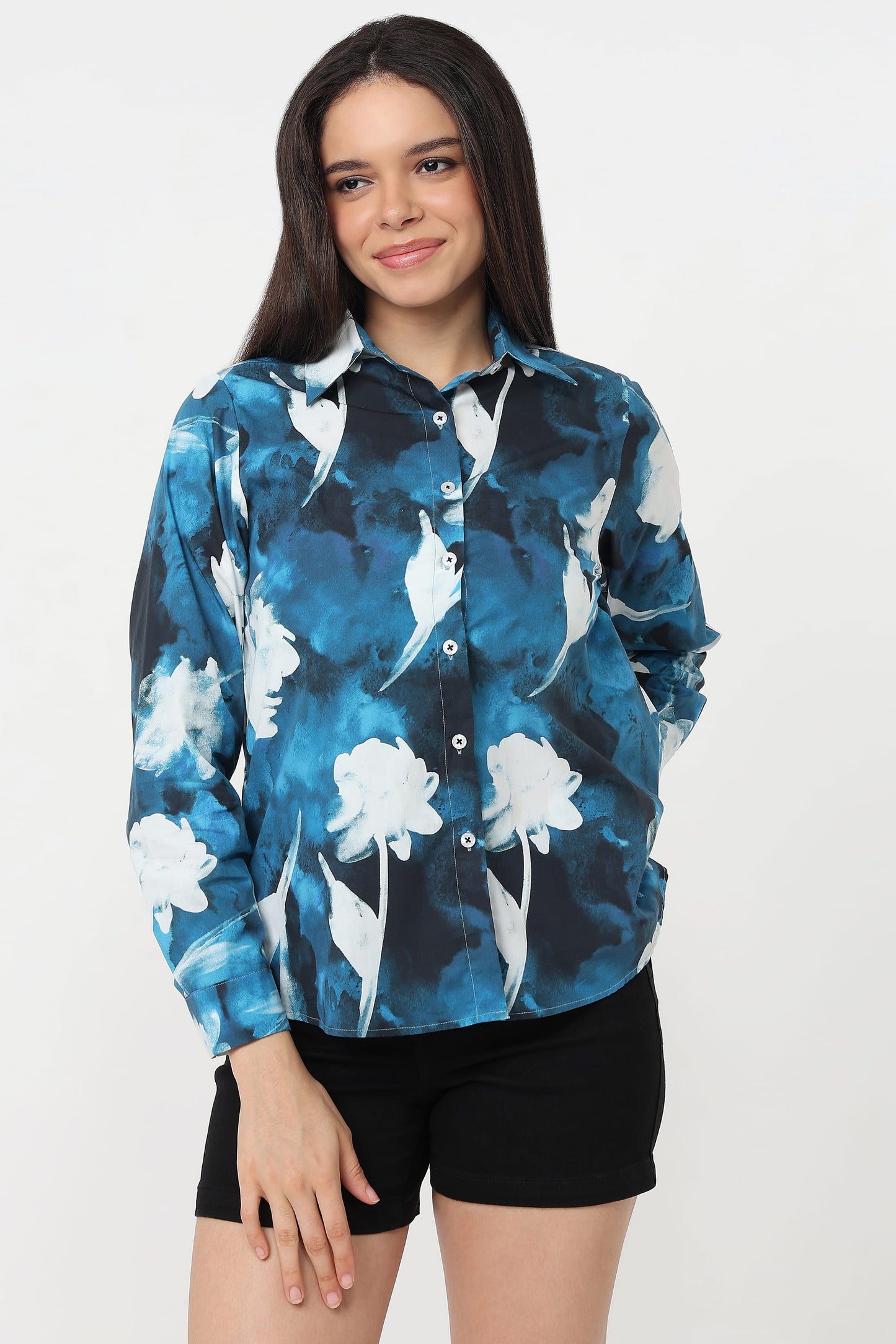 A woman wearing a long-sleeve button-up shirt with a blue, black, and white floral watercolour pattern, paired with black shorts, against a plain white studio background.