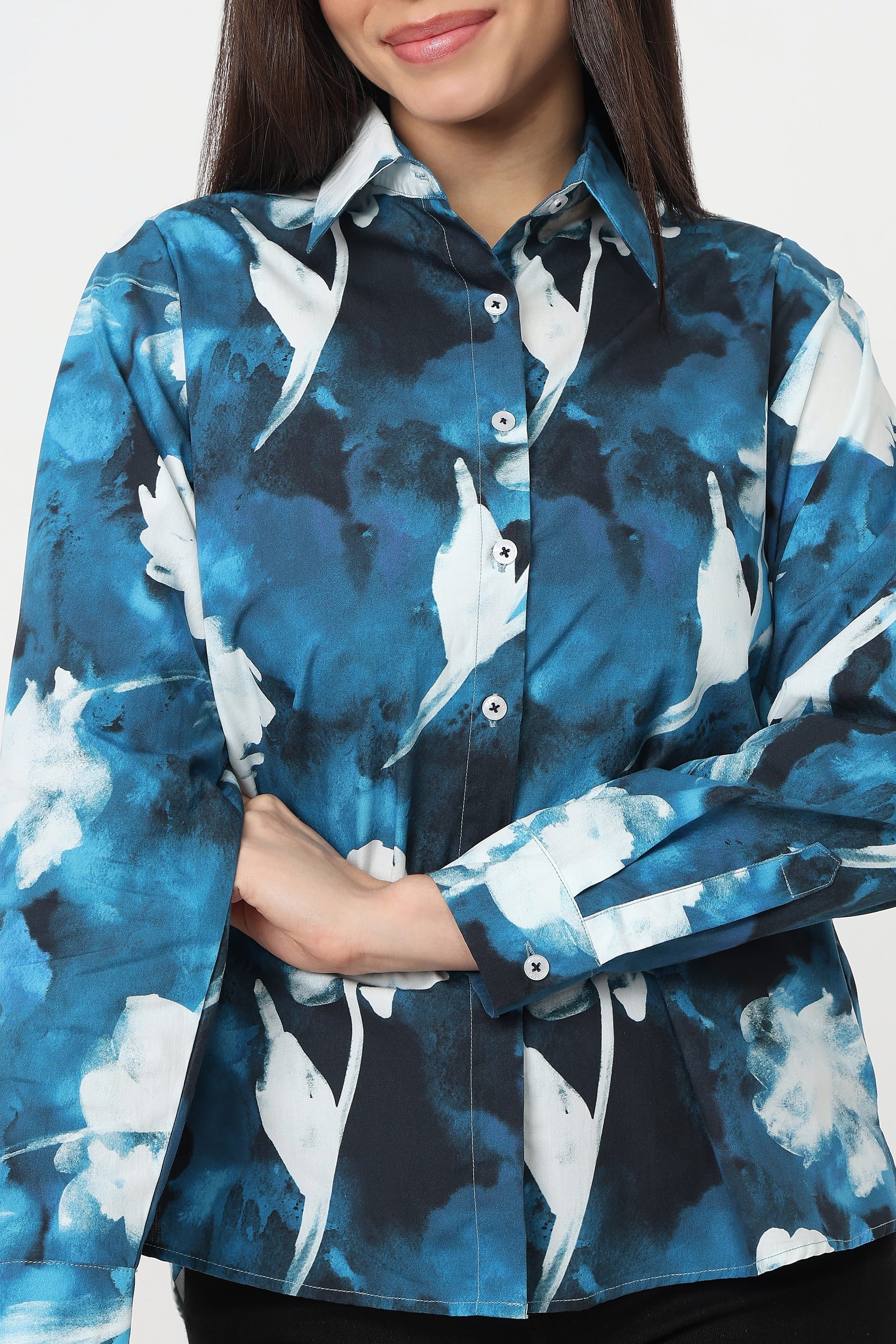 A woman wearing a long-sleeve button-up shirt with a blue, white, and black abstract watercolor-style print, shown from the chest down against a light gray background.