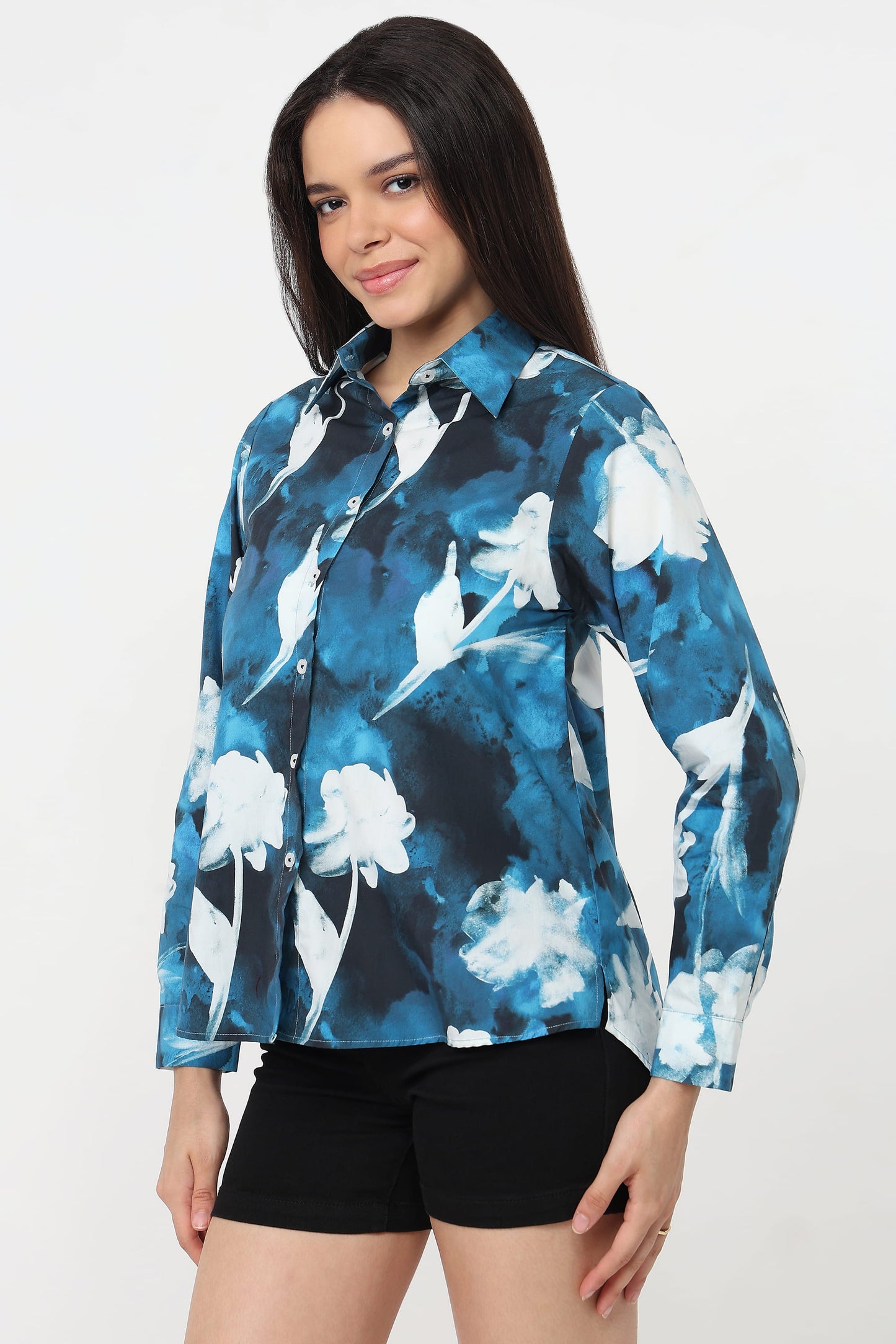 A woman wearing a long-sleeve button-up shirt with a blue, white, and black floral watercolour pattern, paired with black shorts, against a plain white background.