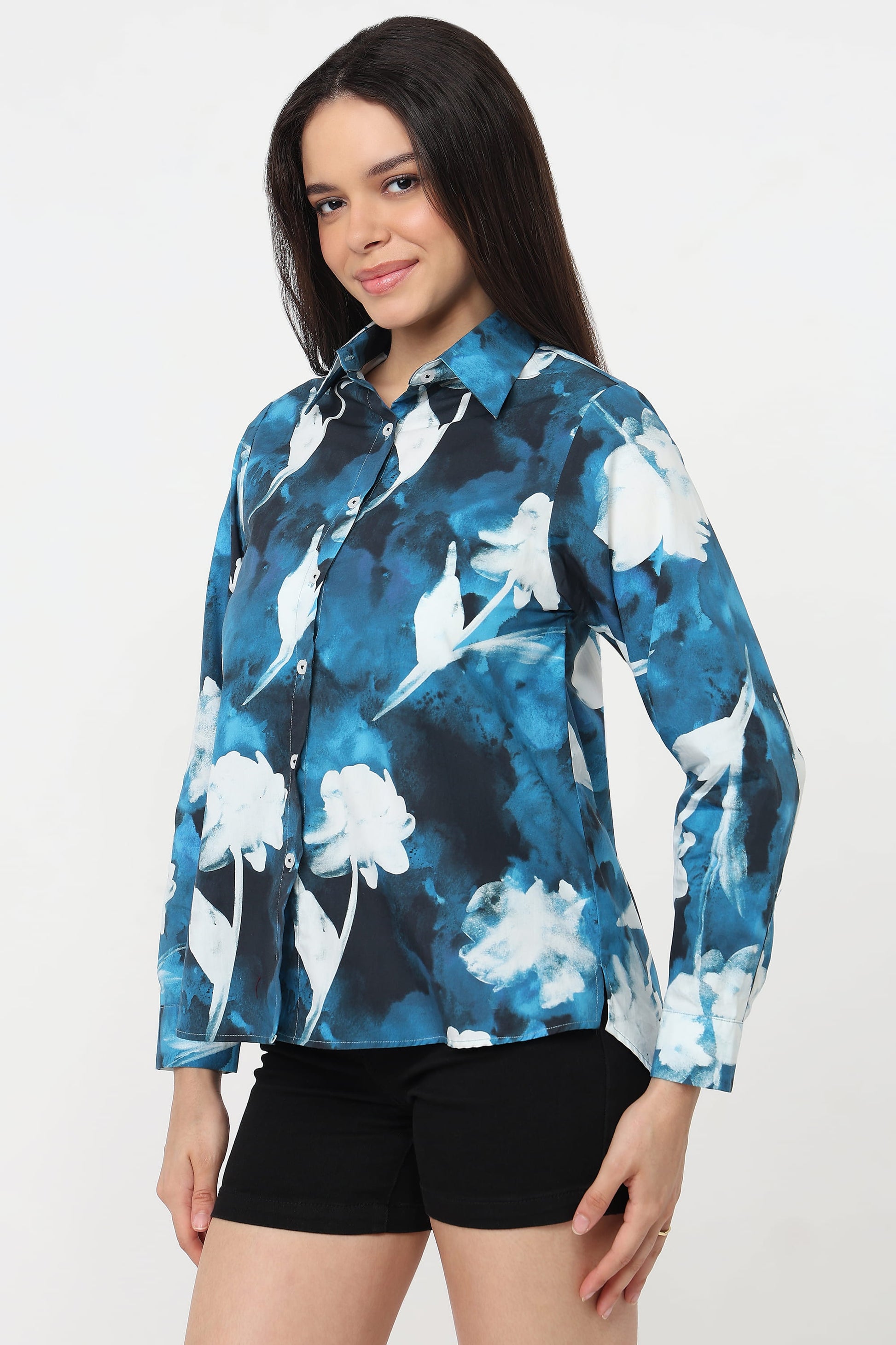 A woman wearing a long-sleeve button-up shirt with a blue, white, and black floral watercolour pattern, paired with black shorts, against a plain white background.