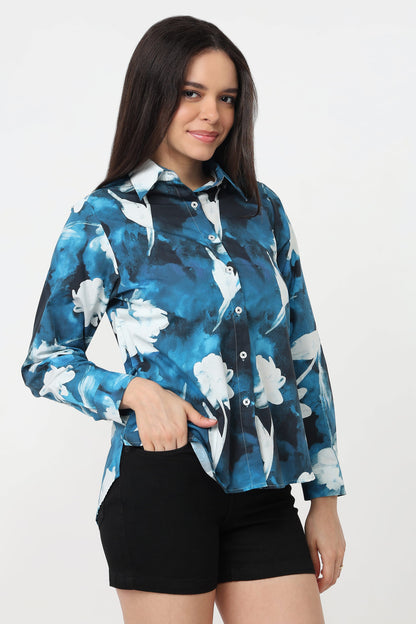 A woman wearing a long-sleeve button-up shirt with a blue and white floral watercolour pattern, paired with black shorts, against a plain white studio background.