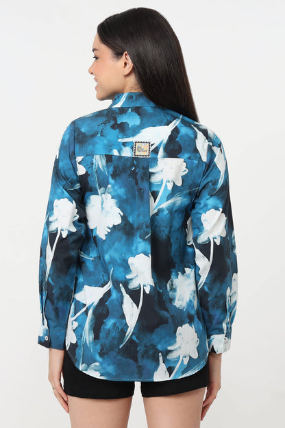 A woman shown from the back wearing a blue and white floral print button-up shirt with black shorts, photographed against a plain light background.
