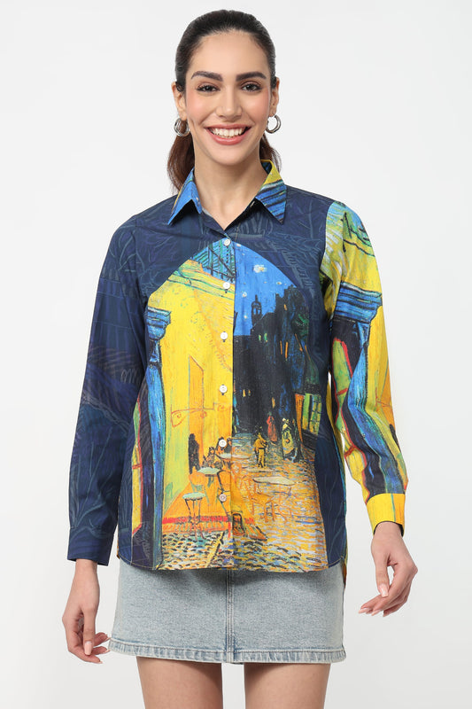 A woman modeling a long-sleeve button-up shirt with a Van Gogh-inspired street scene print in yellow, blue, and black, paired with a light gray denim skirt against a plain white background.