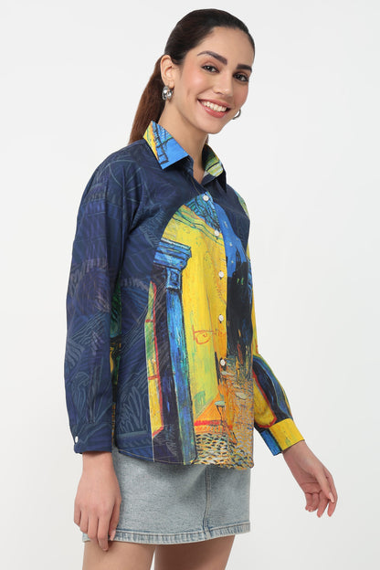 A woman wearing a long-sleeve button-up shirt with a Van Gogh-inspired art print in blue, yellow, and green, paired with a denim mini skirt against a plain white background.