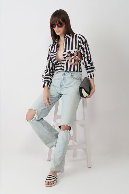 Woman wearing a black and white striped shirt with a graphic design, light blue jeans, and sandals on a white background.