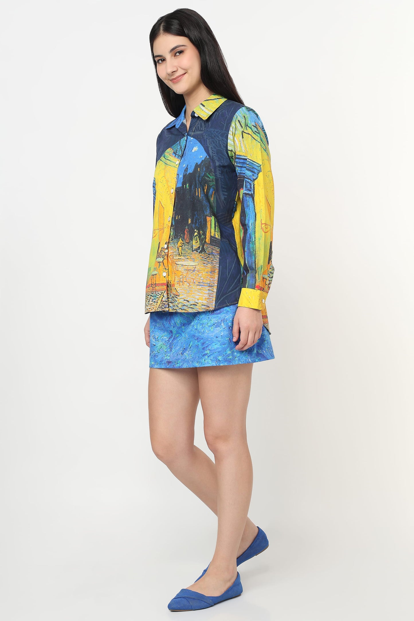 A woman modeling a long-sleeve collared shirt and matching mini skirt set. The shirt features a Van Gogh-inspired print with blue, yellow, and black brushstrokes, paired with a blue patterned mini skirt and blue flats, set against a plain light gray studio background.