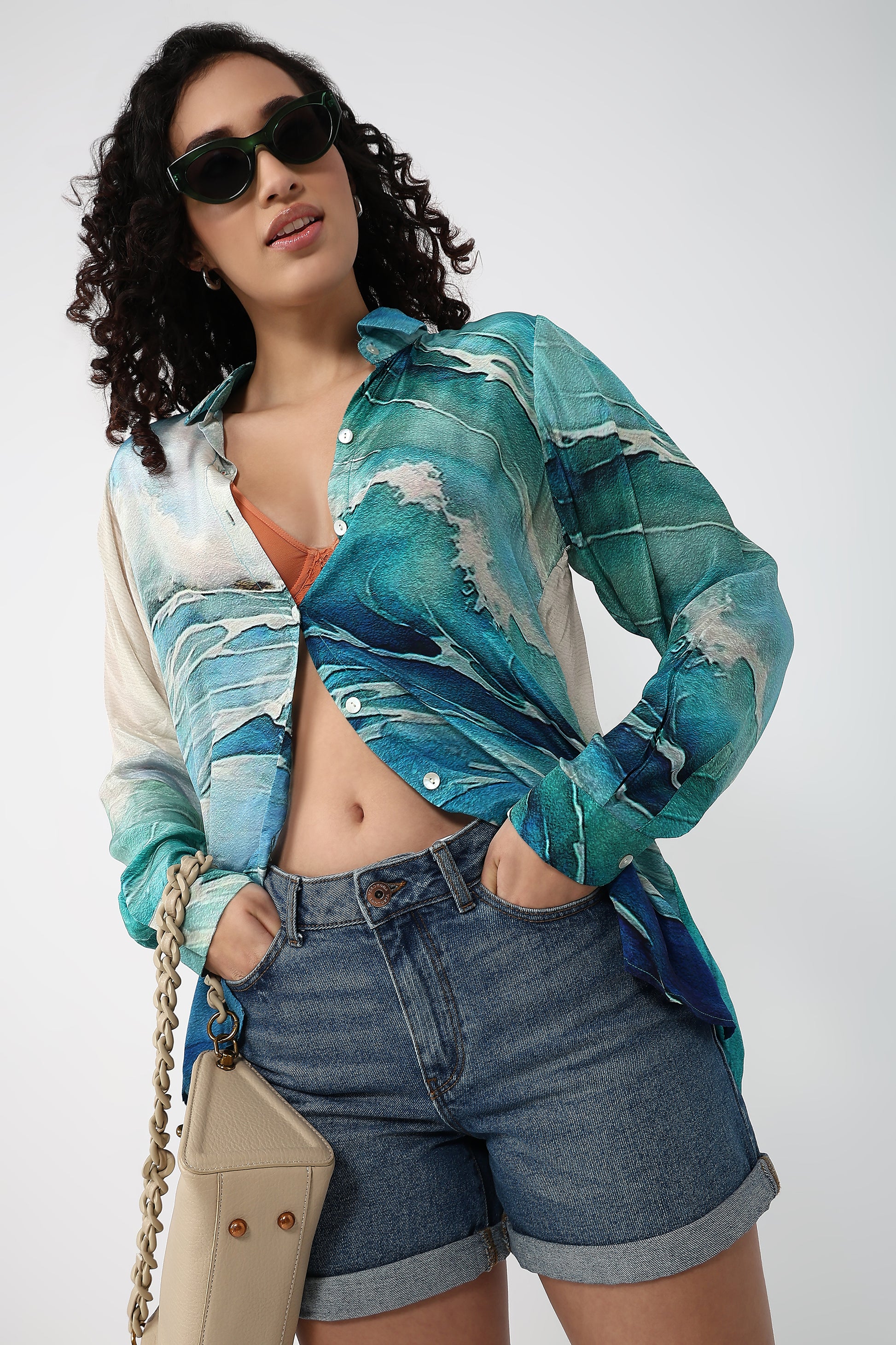 Woman wearing a colorful shirt and denim shorts with sunglasses on a white background