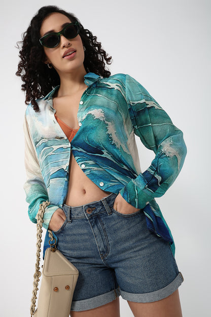 Woman wearing a colorful shirt and denim shorts with sunglasses on a white background