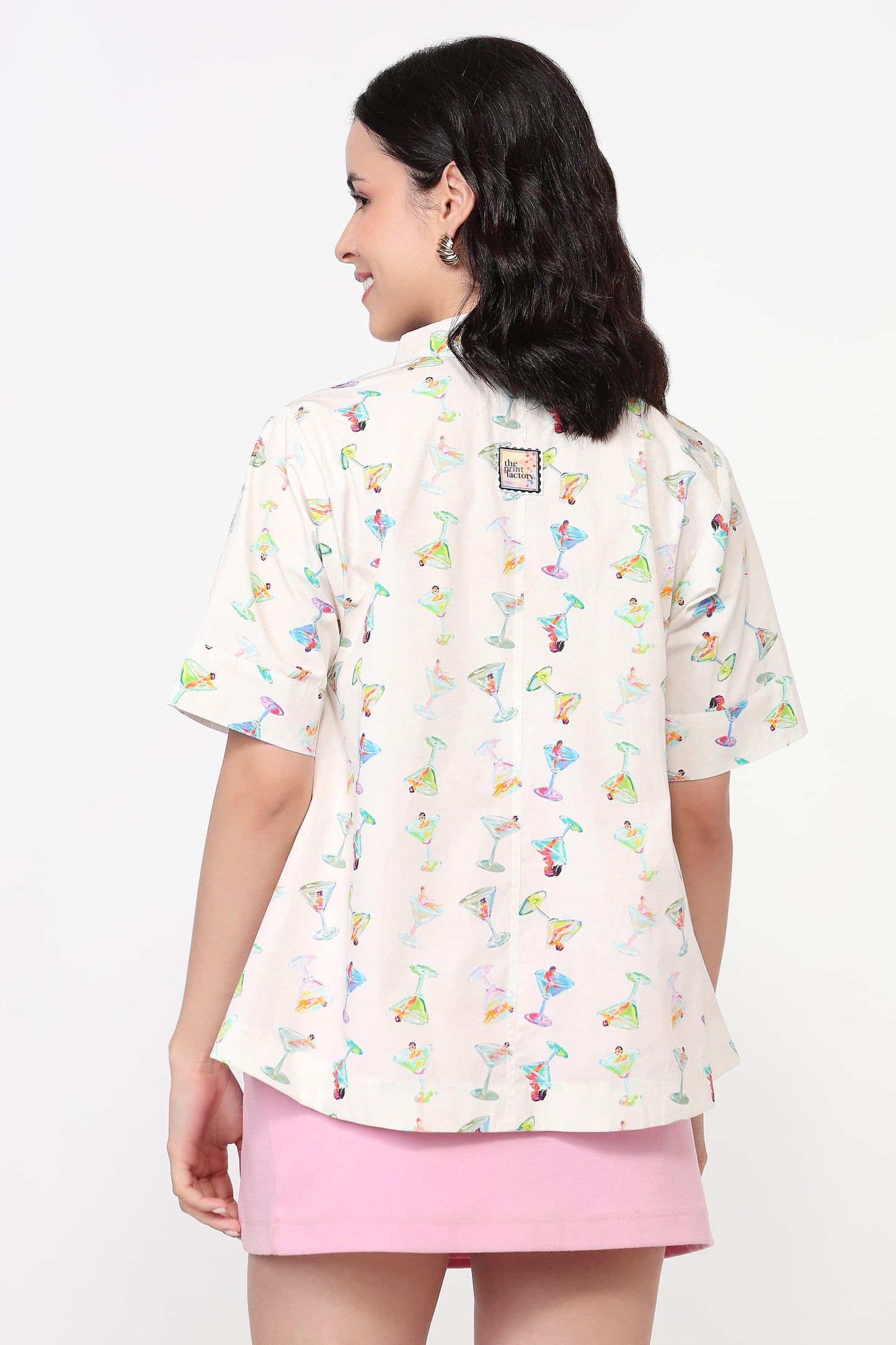 Woman wearing a white blouse with colorful patterns and a pink skirt on a white background