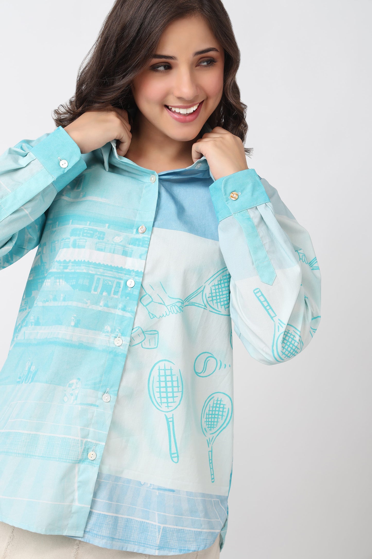 A woman wearing a light blue and white long-sleeve button-up shirt with tennis racket patterns, posing against a light gray background.