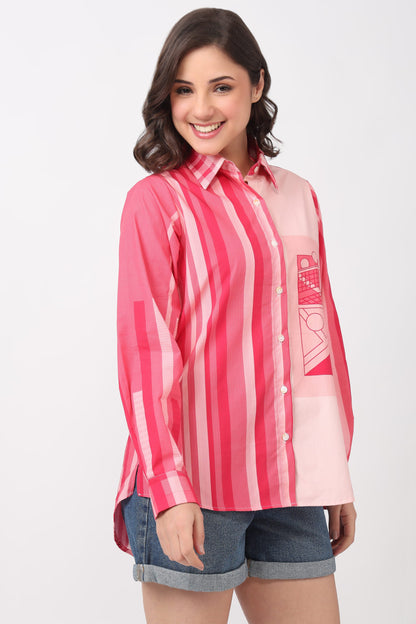 A woman modeling a pink and white vertically striped button-up shirt with a graphic print pocket on the left chest, paired with denim shorts, against a plain light gray background.