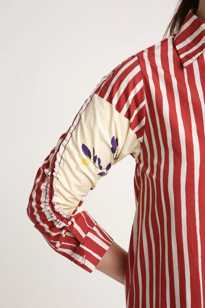 A close-up of a red and white vertically striped shirt with a cream-colored elbow patch featuring purple and yellow floral embroidery, worn by a model.