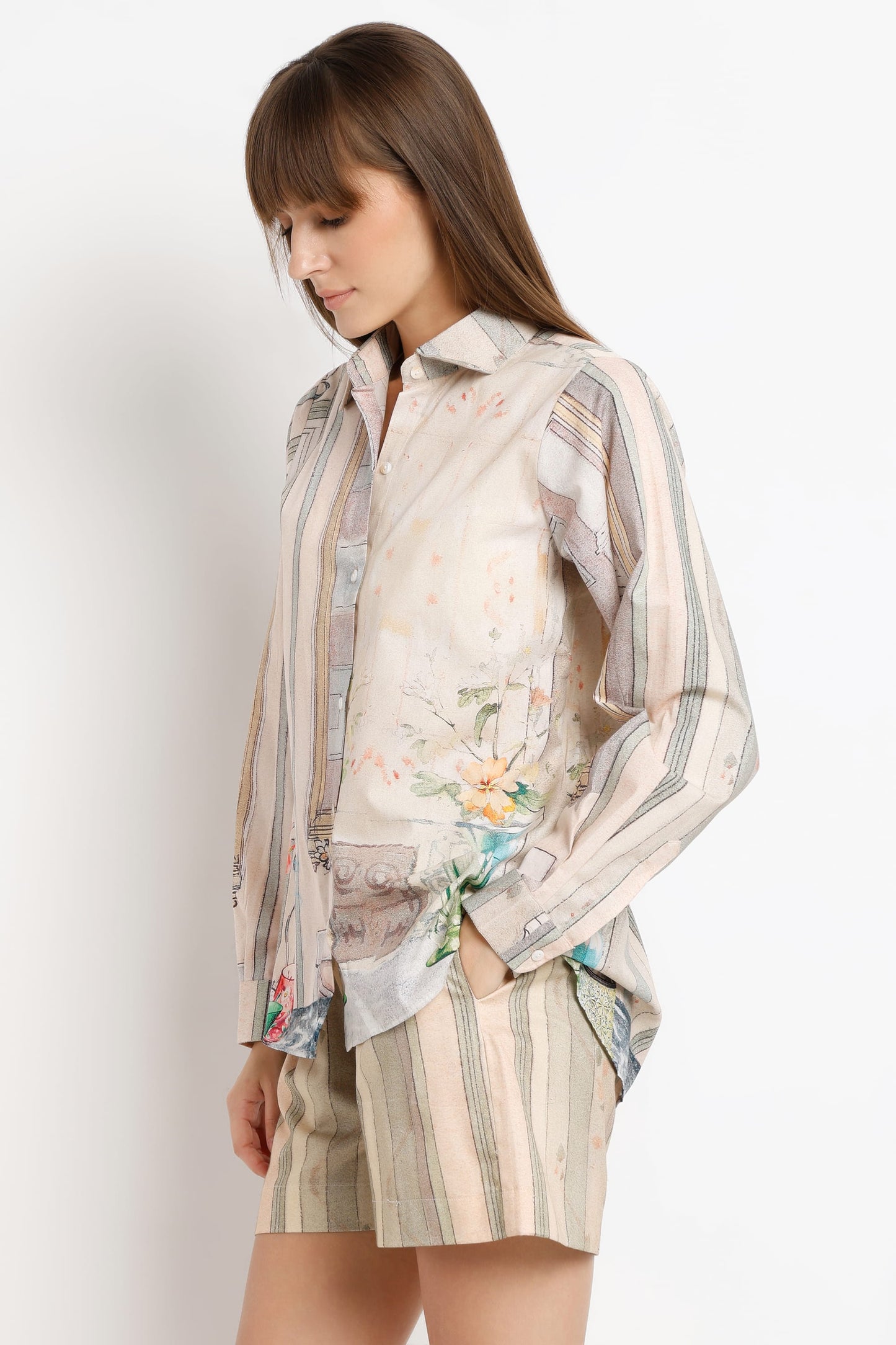 A woman wearing a long-sleeve button-up shirt and matching striped shorts in a soft beige, gray, and floral print, photographed against a plain light background.