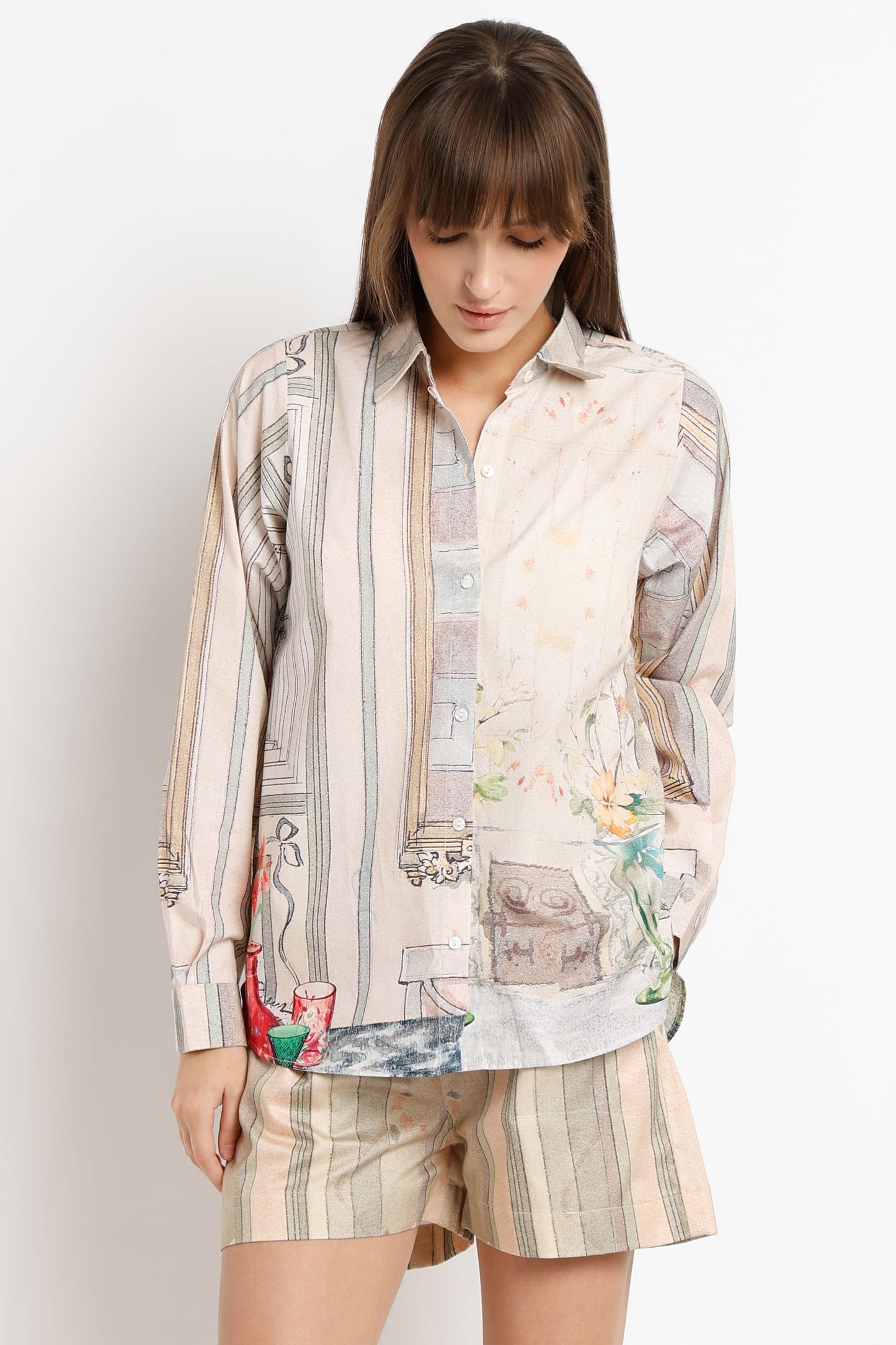 A woman modeling a matching two-piece lounge set featuring a long-sleeve button-up shirt and shorts in a beige and cream patchwork print with subtle illustrations.