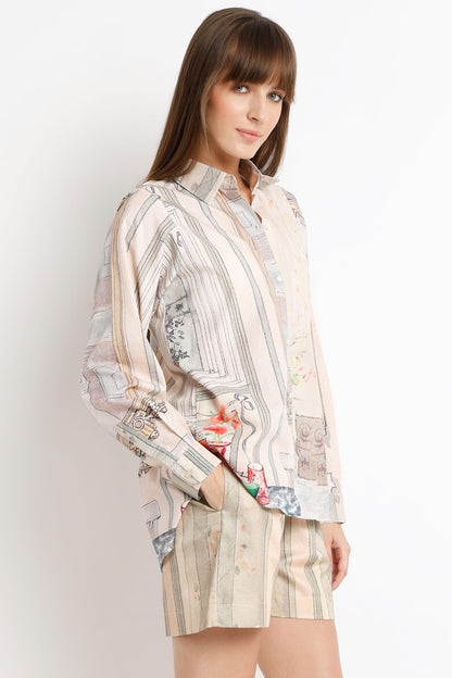 A woman modeling a long-sleeve button-up shirt and matching shorts set. The set features a beige and cream vertical stripe pattern with a whimsical, collage-like print of vintage postcards, illustrations, and small colorful floral accents.