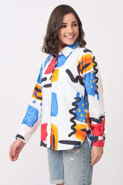 A young girl with shoulder-length brown hair smiling, wearing a white long-sleeve button-up shirt with a colorful abstract geometric print, paired with light-wash denim shorts, against a plain white background.