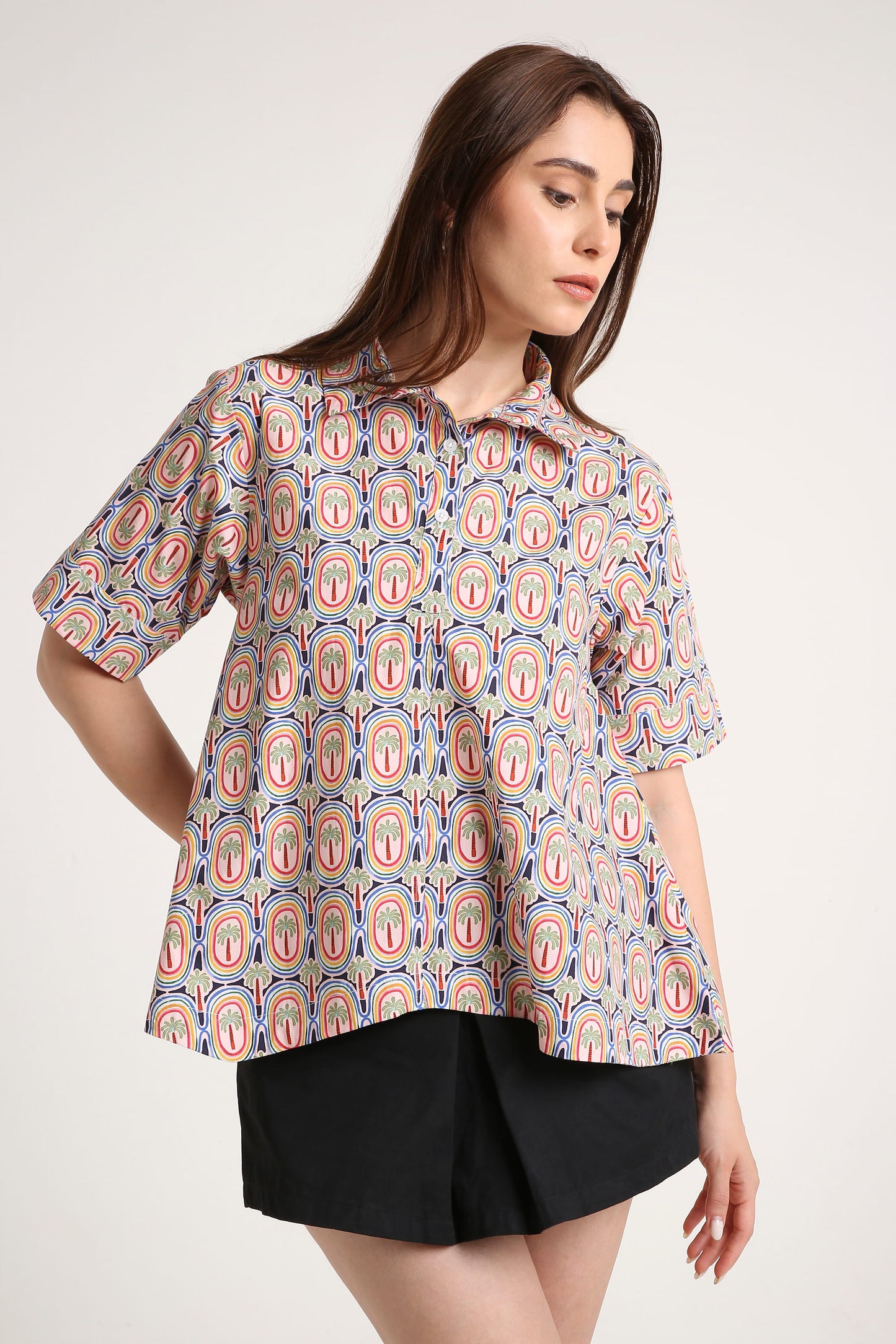 Woman wearing a patterned shirt and black shorts on a white background