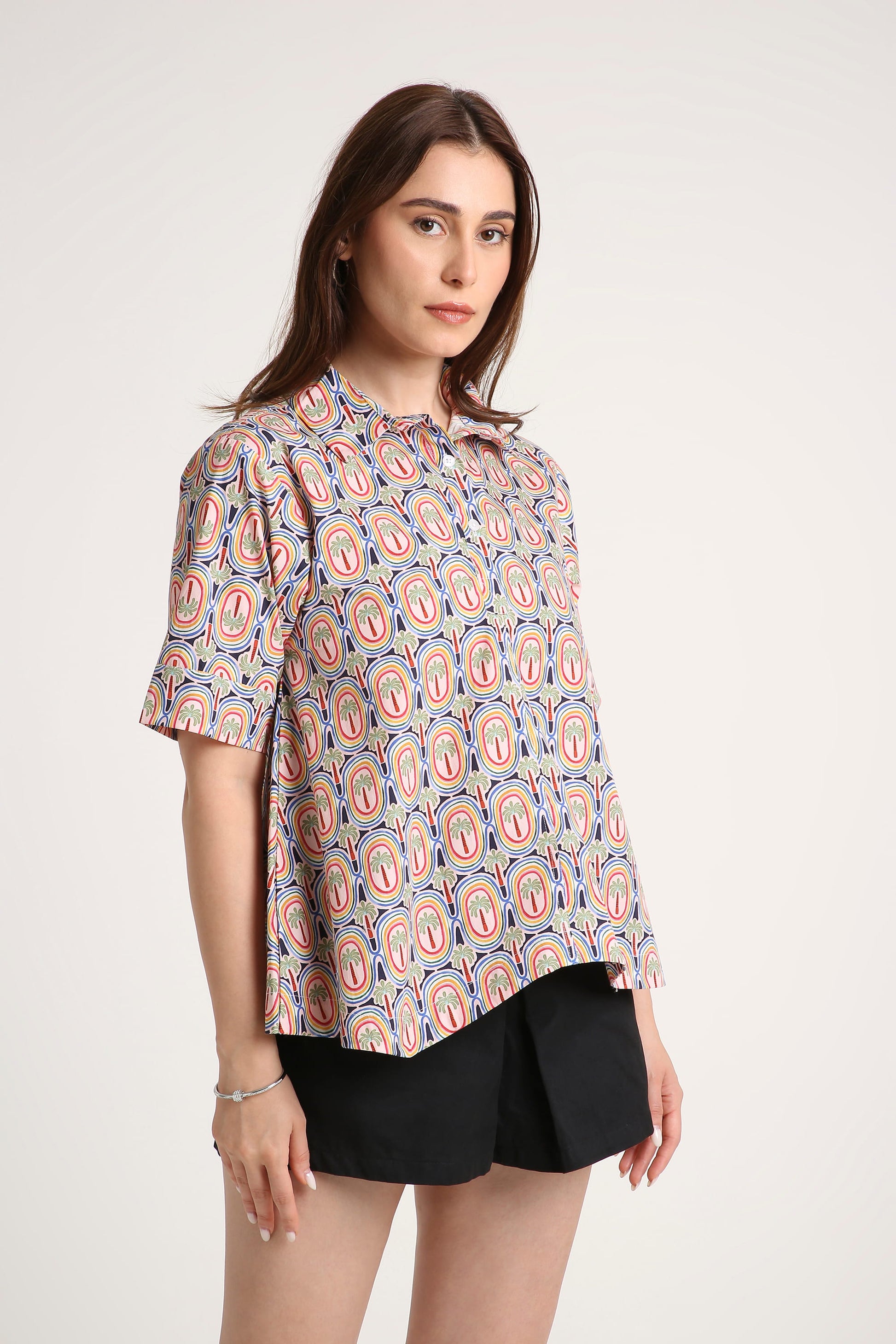 Woman wearing a patterned shirt and black shorts on a white background