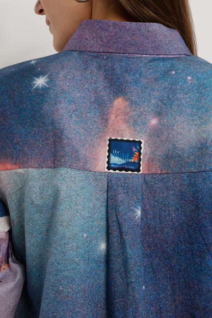 Close-up back view of a person wearing a textured blue and purple space-themed jacket with a small square patch on the upper back.