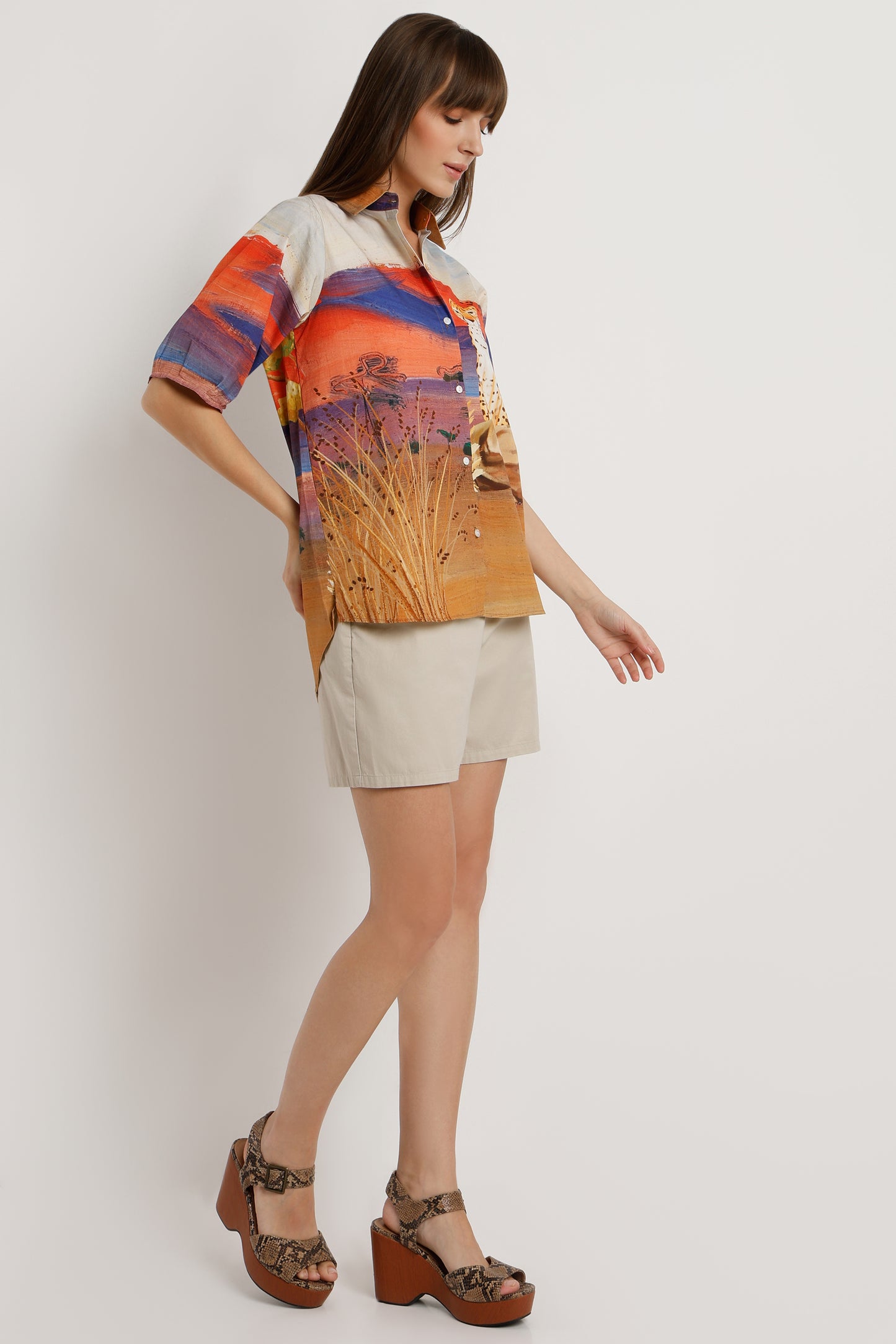 Woman wearing a colorful shirt with a nature print and beige shorts on a white background