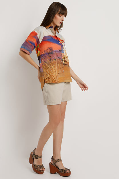 Woman wearing a colorful shirt with a nature print and beige shorts on a white background