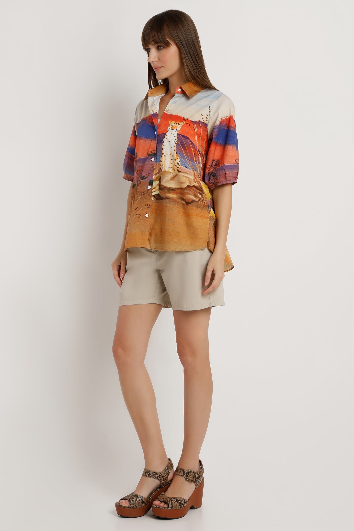 Woman wearing a colorful shirt and beige shorts against a white background