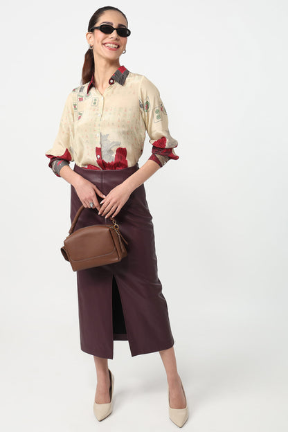 Woman wearing a beige blouse with red accents and a brown skirt, holding a brown handbag on a white background.