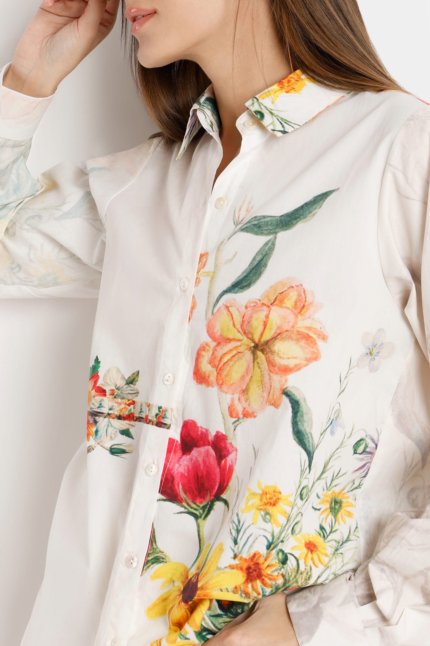 A close-up of a woman wearing a white button-up shirt with a vibrant watercolor-style floral print featuring red, yellow, and orange flowers with green leaves.