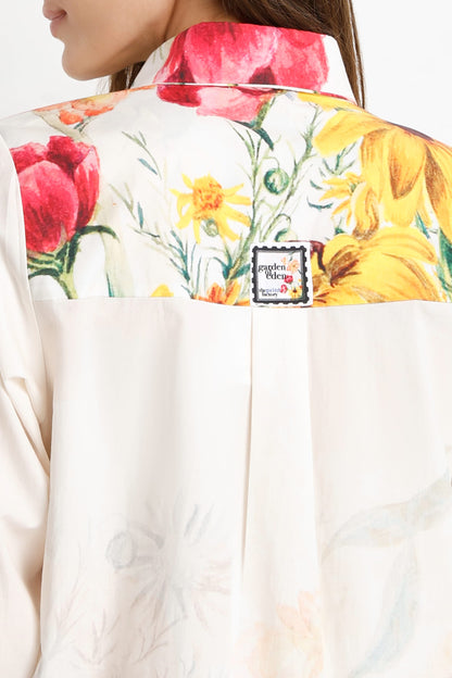 Close-up of the back of a cream-colored jacket with a colorful floral print across the collar and upper back, featuring red tulips, yellow flowers, and green leaves. A small square patch with the brand name is visible near the center.