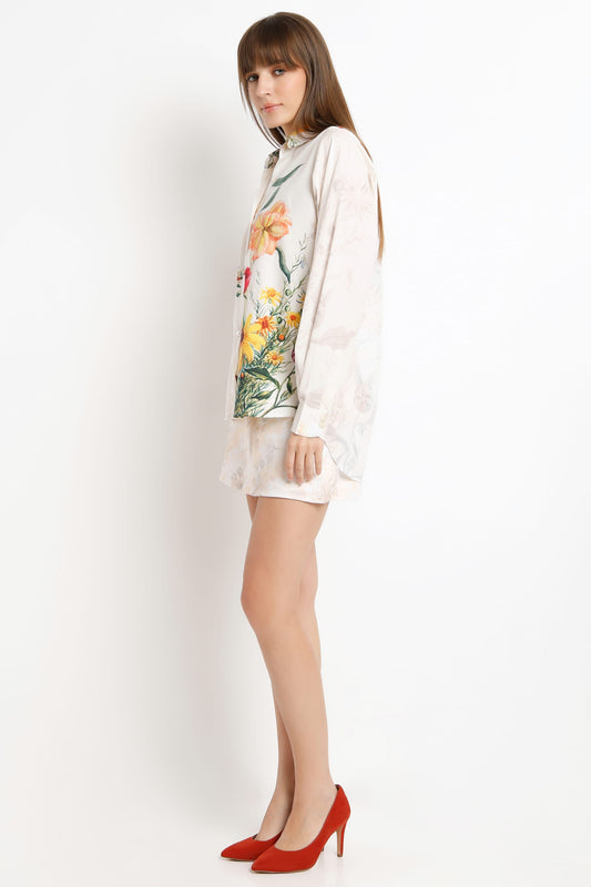 A woman modeling a white long-sleeve shirt with a colorful floral print on the front, paired with red high heels, against a plain white studio background.