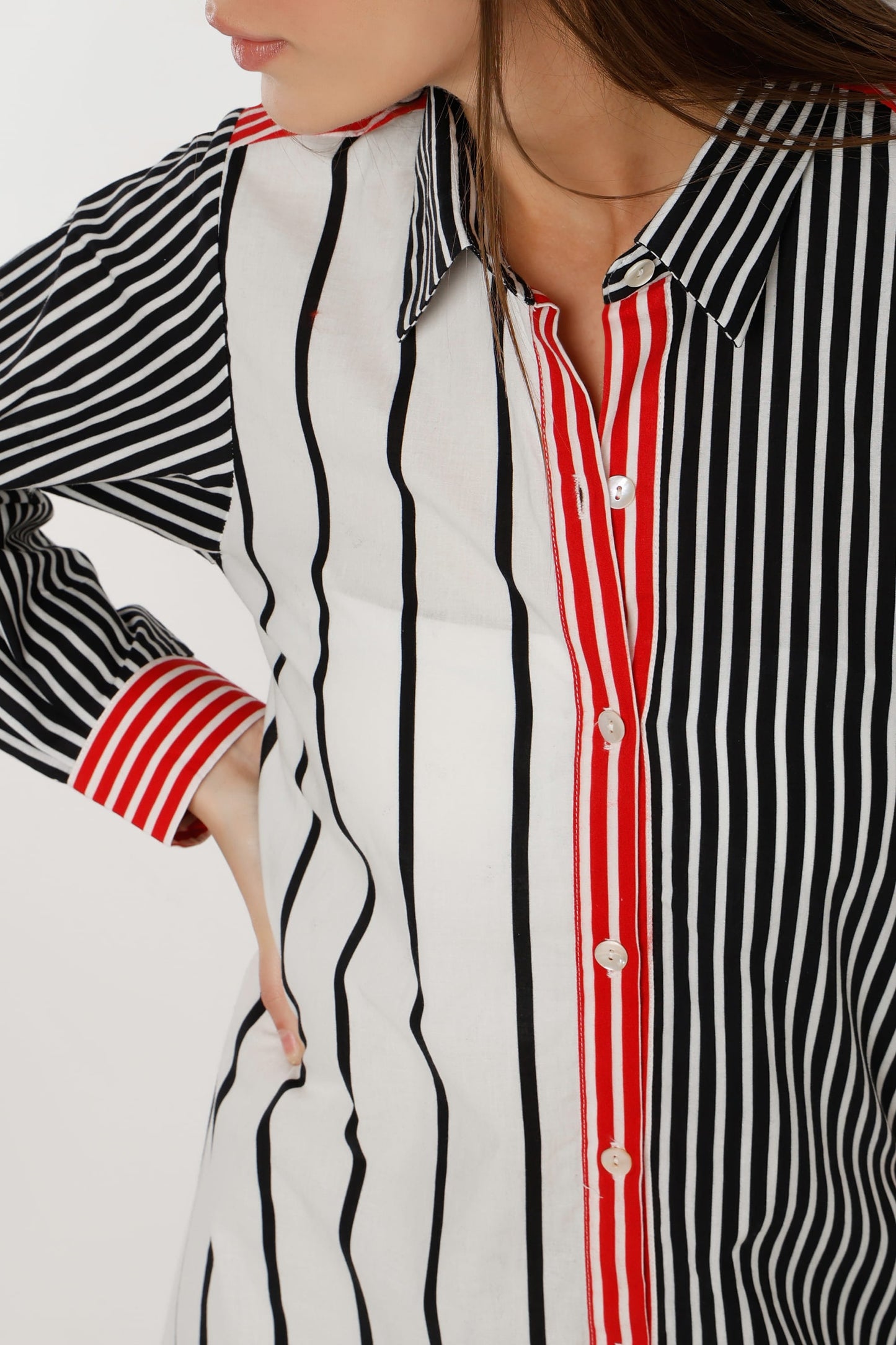 A woman wearing a long-sleeve shirt dress with vertical stripes in black and white, featuring a solid red front placket and red striped cuffs, paired with white sneakers against a light white studio background.