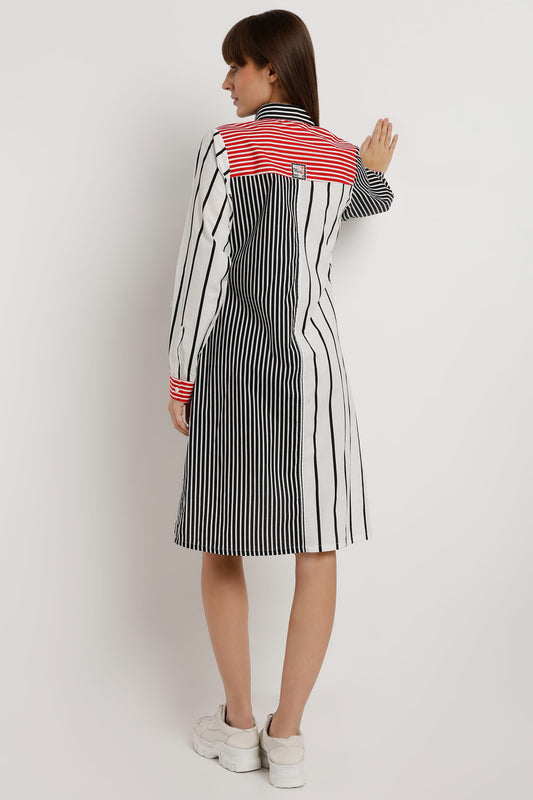 A woman wearing a long-sleeve midi dress from the back, featuring a black and white vertical stripe pattern with a contrasting red and white striped yoke at the collar and red striped cuffs, set against a plain light white background.