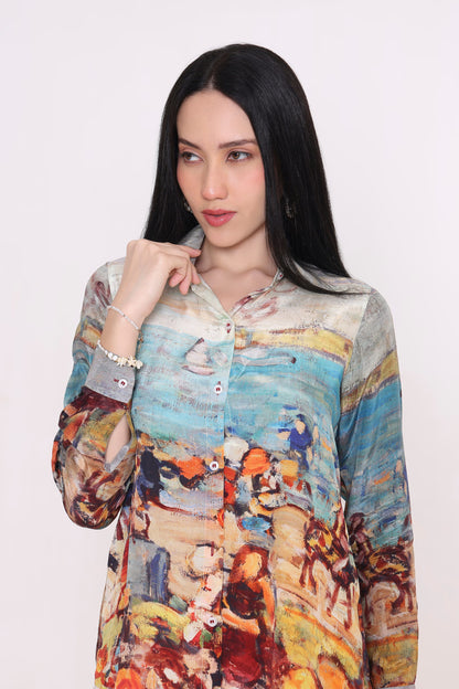 A woman with long black hair wearing a long-sleeve button-up shirt with an abstract, painterly multicolor print in shades of blue, orange, yellow, and brown, posed against a plain light background.