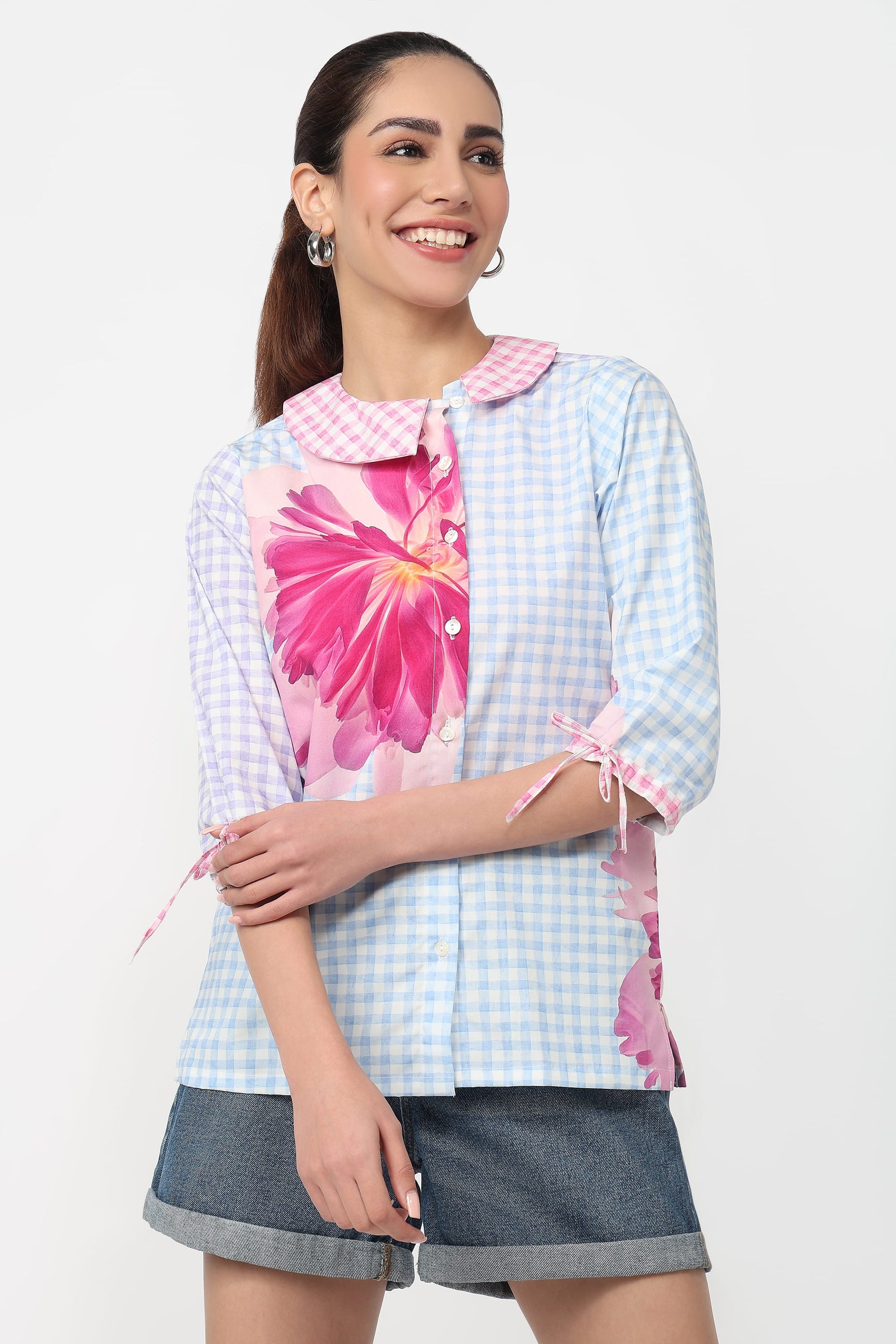 Woman wearing a light blue checkered shirt with pink floral accents on a white background