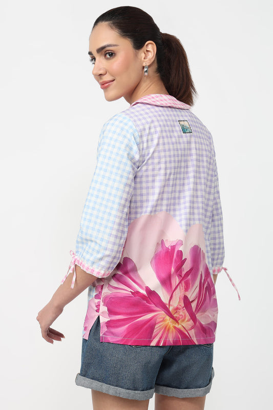Woman wearing a checkered shirt with floral design on the back, standing against a white background.