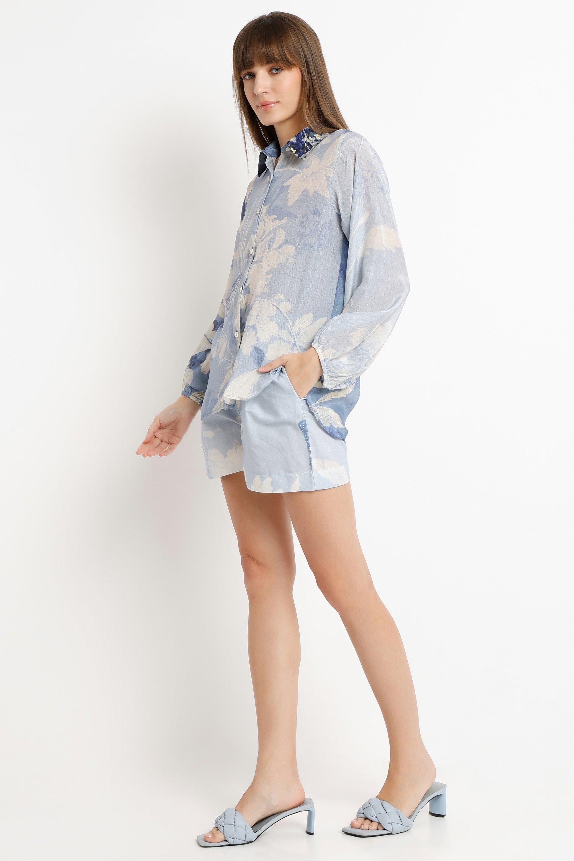 Woman wearing a light blue floral shirt and shorts on a white background