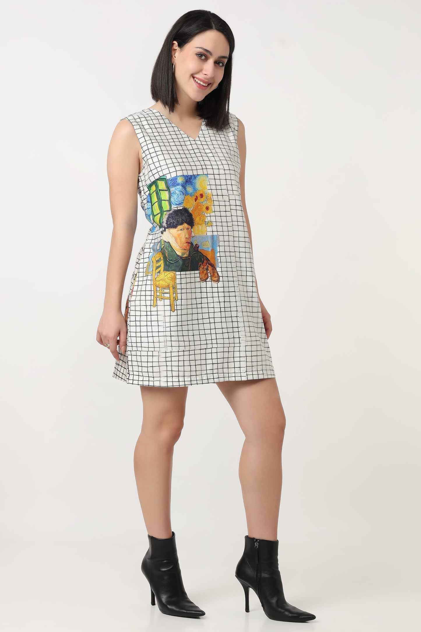 A woman wearing a sleeveless mini dress with a black and white grid pattern and a colourful graphic print on the front, paired with black ankle boots, against a plain light background.