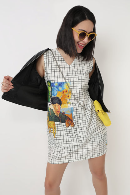 A woman modeling a sleeveless white V-neck dress with a black grid pattern and a colorful graphic print on the front, styled with a black jacket draped over her shoulders and a small yellow crossbody bag.