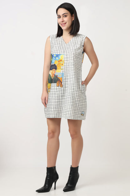 A woman wearing a sleeveless mini dress with a black and white grid pattern and a colourful graphic print on the front, paired with black ankle boots, against a plain light background.