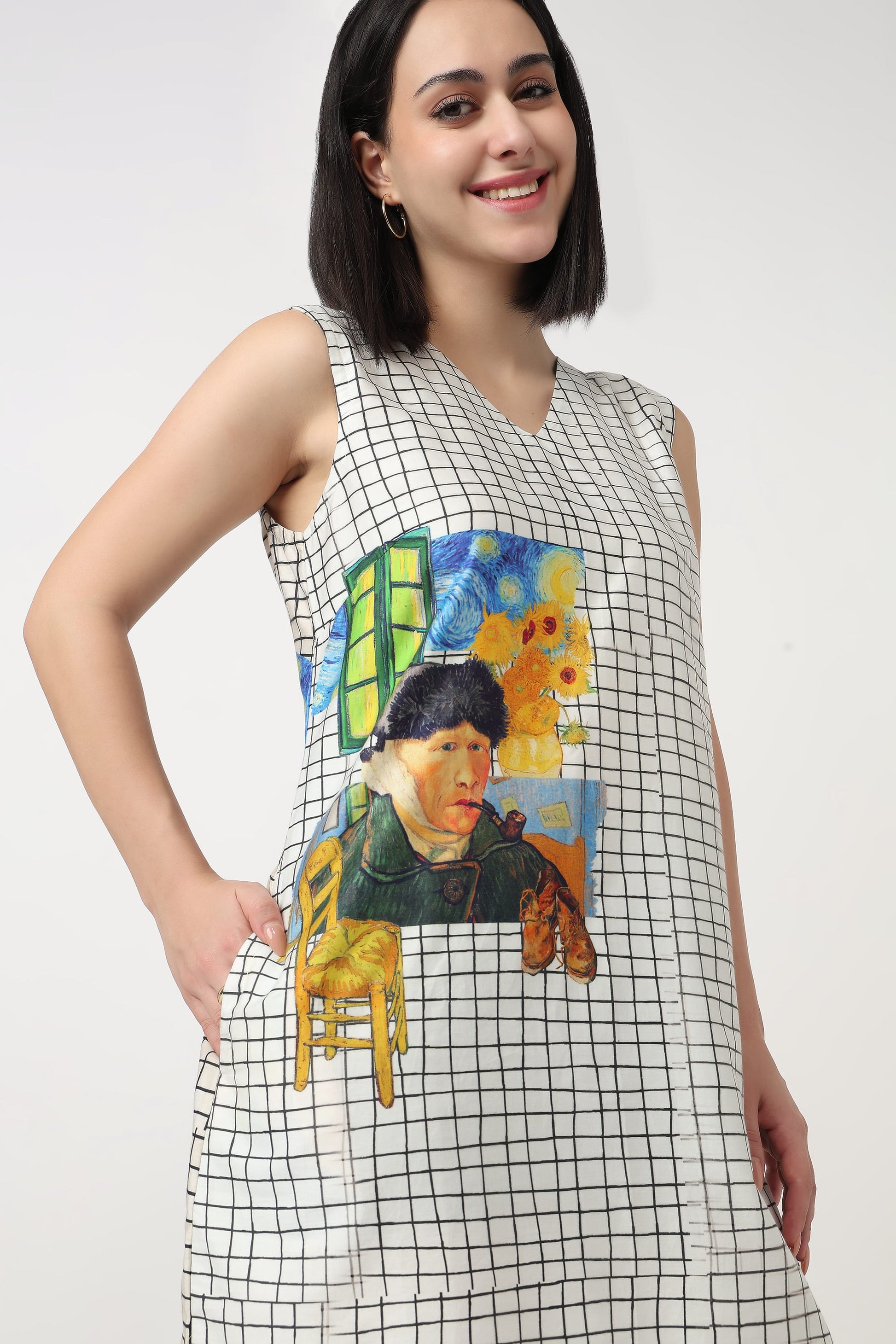 A woman wearing a sleeveless white V-neck dress with a black grid pattern and a large Van Gogh-inspired painting graphic on the front, set against a plain light gray studio background.