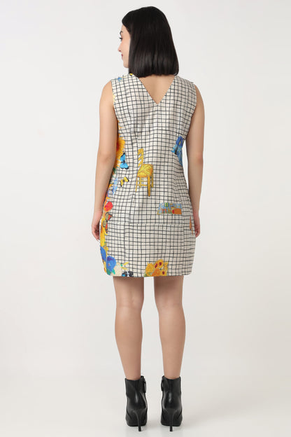 A woman viewed from the back wearing a sleeveless mini dress with a black and white grid pattern and colorful giraffe illustrations, paired with black ankle boots, against a plain light background.